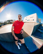 © Studio Marmellata - Male runner in a bright red shirt leans casually against a modern architectural structure under a clear blue sky on a sunny day, exuding confidence and style in a contemporary setting.