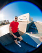 © Studio Marmellata - Male runner in a bright red shirt leans casually against a modern architectural structure under a clear blue sky on a sunny day, exuding confidence and style in a contemporary setting.