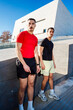 © Studio Marmellata - Two male runners one in red and one in black, pose confidently near a modern architectural building under a clear blue sky on a sunny day, exuding style and camaraderie.