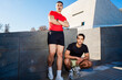 © Studio Marmellata - Two male runners one in red and one in black, pose confidently near a modern architectural building under a clear blue sky on a sunny day, exuding style and camaraderie.