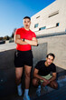 © Studio Marmellata - Two male runners one in red and one in black, pose confidently near a modern architectural building under a clear blue sky on a sunny day, exuding style and camaraderie.