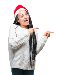 Wall Mural - Young braided hair african american girl wearing christmas hat over isolated background smiling and looking at the camera pointing with two hands and fingers to the side.