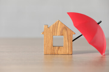 Wall Mural - Property insurance. Wooden house figure and small umbrella on table, space for text