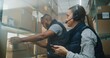 © Framestock - Multiethnic Warehouse Associates Working in Sorting Center of Delivery Service: Female Employee in Headset Scans Cardboard Parcels with E-Commerce Online Goods Using Smartphone, Checks Information.
