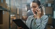 © Framestock - Female Customer Support Specialist in Logistics, Manager Talks with Client on Phone, Uses Tablet Computer. Warehouse Employee Working in Background. Delivery Service of E-Commerce Store. Close Up.