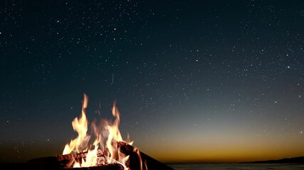 Wall Mural - a bonfire burns at night against the background of mountains and sea with bright stars..