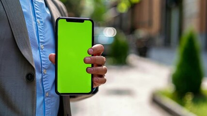 Poster - A person in a suit stands confidently on a city street, displaying a smartphone with a bright green screen.