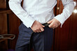 © Vasil - A man in a white shirt is adjusting his belt. Concept of formality and attention to detail, as the man is making sure his pants are properly fastened