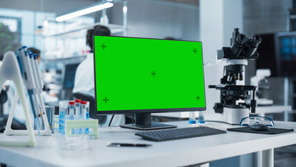 Aufkleber - Desktop Computer with Green Screen Mock Up Display Standing on a Table in a Science Laboratory Next to a Microscope and Test Tubes with Biological Samples. Anonymous People Working in the Background