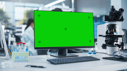 Aufkleber - Desktop Computer with Green Screen Mock Up Display Standing on a Table in a Science Laboratory Next to a Microscope and Test Tubes with Biological Samples. Anonymous People Working in the Background