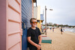 © Austockphoto - Boy in sunglasses smiles against colorful beach huts on lively sandy coastline