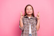 © deagreez - Charming young girl in casual checkered shirt with crossed fingers on pink background showing hope and positivity