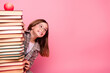 © deagreez - Adorable schoolgirl posing with a stack of books on a pink background, expressing joy