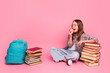 © deagreez - Young girl enjoying an apple while sitting with a backpack and books against a pink backdrop, expressing education and lifestyle.