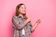 © deagreez - Young girl pointing sideways with a smile, dressed in a trendy checkered shirt against a pink background conveying happiness and lighthearted energy.
