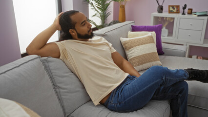 Young man relaxing indoors in a modern living room, characterized by a cozy apartment style, wearing casual attire and showcasing a peaceful ambiance.