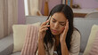 © Krakenimages.com - Hispanic woman talking on the phone in her living room looking stressed and concerned with hands on her head