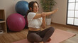 © Krakenimages.com - Woman stretching on yoga mat at gym surrounded by exercise balls and plants, embodying wellness and tranquility in a clean indoor sports center.
