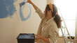 © Krakenimages.com - Woman painting wall blue with roller in bright home interior, showcasing diy project in new apartment with ladder and wearing casual attire, exuding creativity and focus.