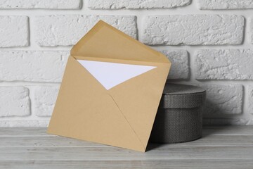 Wall Mural - Kraft paper envelope with letter and box on wooden table near white brick wall. Mockup for design