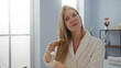 © Krakenimages.com - Woman brushing long blonde hair in a serene spa salon wearing a white bathrobe, illuminated by natural indoor light in a wellness center