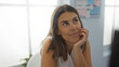© Krakenimages.com - Young woman with brunette hair sitting in an office room, looking thoughtful and attractive, with a soft smile in an indoor workplace setting