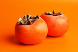 two gray persimmons on an orange background