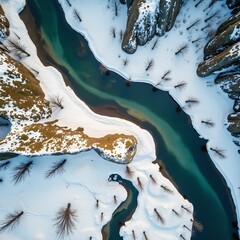 Aufkleber - high-angle view of a snowy landscape with a river flowing through it. The river is surrounded by mountains with some trees and rocky outcrops visible.
