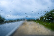 © marinv - Raindrops on Windshield with a Blurred Countryside Road Under Cloudy Skies