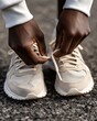 © Espresso - A close-up of a Black male tying his light beige athletic shoes on a textured asphalt surface.