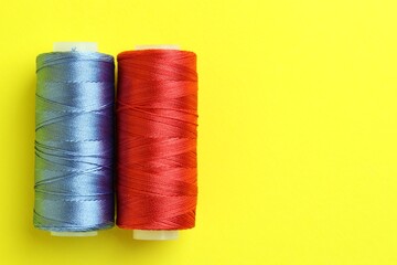 Spools of colorful sewing threads on yellow background, top view. Space for text