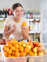 Wall Mural - Young woman buyer choosing fresh fruits tangerines in grocery store