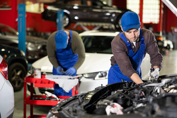 Wall Mural - Professional mechanic man in uniform repairing car in auto repair shop garage