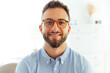 © Kateryna - Close-up portrait of a smiling, successful man in glasses and a blue shirt, confident and professional appearance. Attractive, positive caucasian or arabian male stand in the office, looking at camera