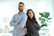© Kateryna - A confident man in a blue shirt and glasses stands next to a brunette beautiful woman, they standing in a modern office with arms crossed, smiling at the camera, showcasing teamwork and confidence