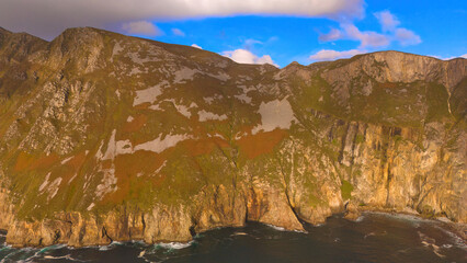 Wall Mural - Slieve League in Donegal Ireland - the highest cliffs in Europe - Experience a breathtaking view of rugged cliffs merging with the calm ocean under a partly cloudy sky