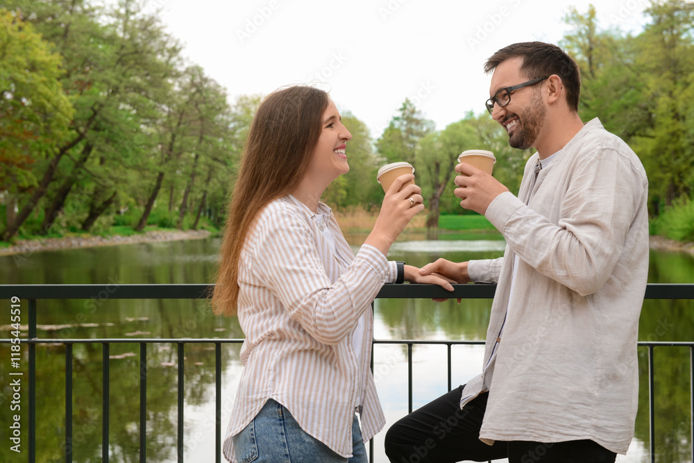 Beautiful happy couple speaking and drinking coffee on bridge in park