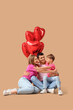 © Pixel-Shot - Little boy with his parents and balloons hugging on beige background. Valentine's Day celebration
