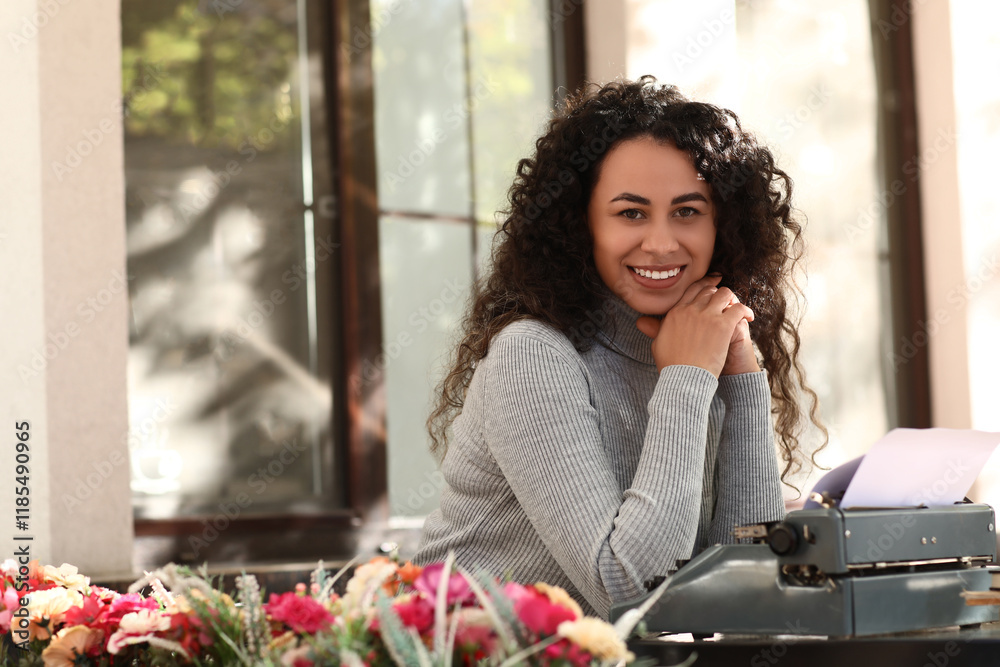 Young African-American author with typewriter sitting at table in street cafe