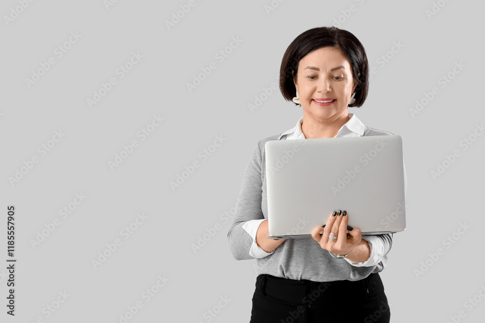 Mature businesswoman working with laptop on light background
