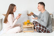 © Pixel-Shot - Young couple with sandwiches having breakfast in bedroom