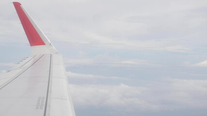 Wall Mural - view through aircraft window with plane's winglet over blue sky with white fluffy clouds from airplane flight fly over the clouds in a sunny day with cloud moving
