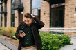 © dikushin - Surprised young man standing in urban street, holding smartphone and reacting with astonishment to some unexpected news just received, looking to phone screen with happy excited expression.