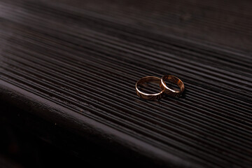 two gold wedding rings lying next to each other on a dark wooden surface with a texture in the form 