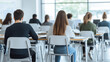 © pattozher - Students Focused in Classroom:  A rear view of a diverse group of students attentively seated at desks in a modern classroom, focused on their studies.