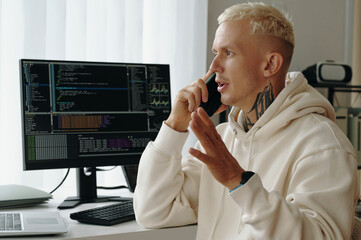 Young programmer discussing computer software on the phone while working in office