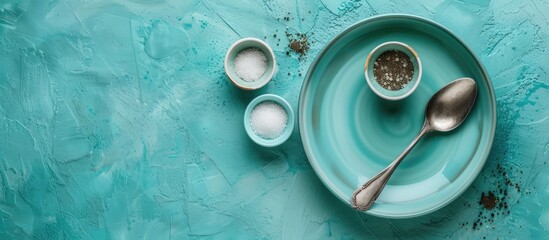 Fototapete - Dinner table with no food A blue ceramic plate and a silver spoon are placed on a turquoise table accompanied by a bowl of salt and pepper Top view. with copy space image