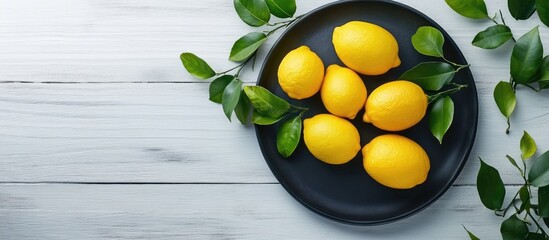 Fototapete - Fresh ripe juicy lemons on a black plate with green leaves on a white wooden table from a top view copyspace for your text