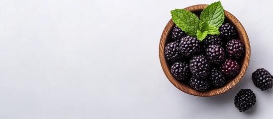 Aufkleber - Blackberries alongside a mint leaf in a wooden bowl featuring copy space for text A fresh and delicious blackberry set against a white background Top view