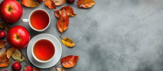 Poster - Autumn colors Red apples a cup of tea and leaves on a gray concrete background Flat lay. with copy space image. Place for adding text or design